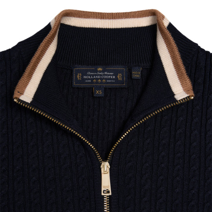 Close up of a navy jumper with a gold zip and brown/cream collar detailing against a white background. 
