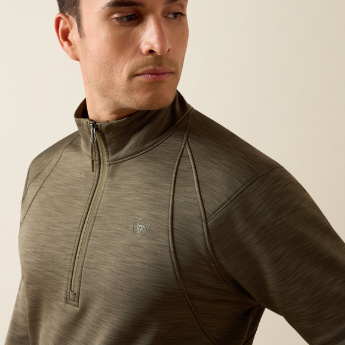 Ariat Men's Team EQ 1/2 Zip Pullover Varient Kalamanta. Man wearing a khaki long sleeve top with 1/2 zip detailing and an Ariat logo on a beige background. 