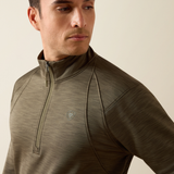 Ariat Men's Team EQ 1/2 Zip Pullover Varient Kalamanta. Man wearing a khaki long sleeve top with 1/2 zip detailing and an Ariat logo on a beige background. 