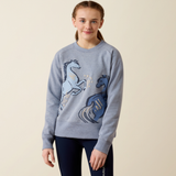 Ariat Youth Martine Sweatshirt AW26 Varient Blue Grey Lets Play. Girl wearing Blue jumper with two horses and black leggings on a beige background.