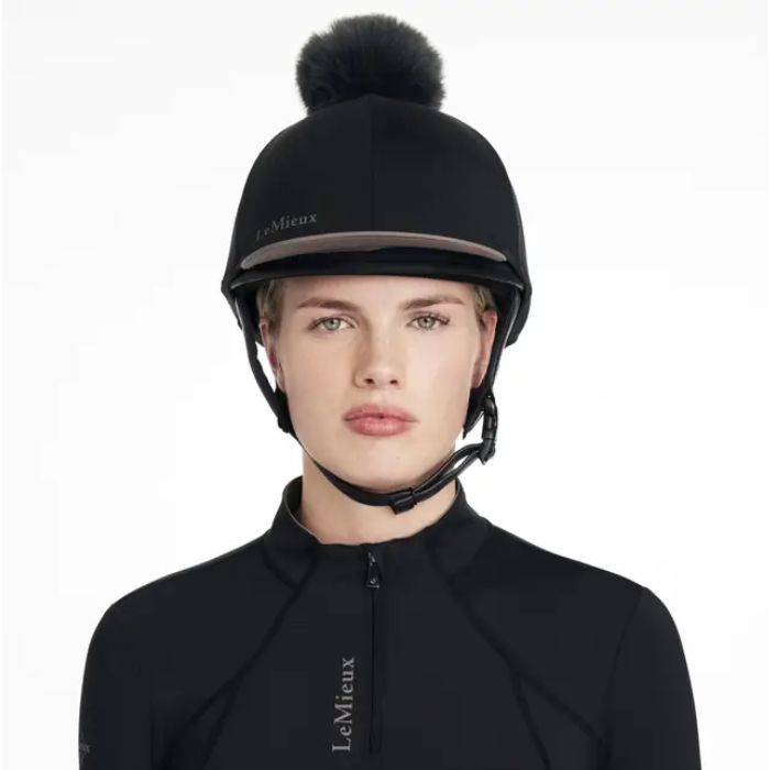 Person wearing a black equestrian helmet with a pom-pom on a white background