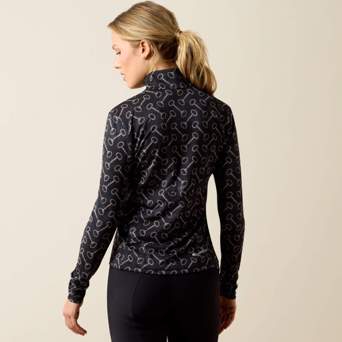 Ariat Ladies Lunaveil 1/2 Zip Long Sleeve Base Layer Variant Black French Link Print. A woman shown from the back wearing a long-sleeve athletic top with a dark navy base and an allover white abstract pattern, paired with black leggings, against a plain beige studio background.