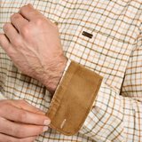 Dubarry Men's Corrib Shirt Variant Ochre. Close-up of a man's hands adjusting the cuff of a brown suede button-up shirt over a cream and tan plaid dress shirt.