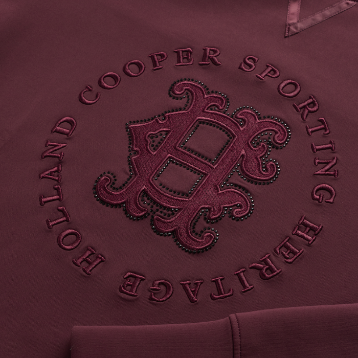 Holland Cooper Cranborne Crystal Crew Variant Mulberry. Close-up of a maroon hoodie featuring an embossed circular design with the text 'HOLLAND COOPER SPORTING HERITAGE' and a large decorative monogram in the center.