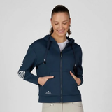 Pikeur AW26 Athleisure Zip Hoody Variant Pine Green. A woman wearing a navy blue zip-up hoodie with a drawstring hood, front pockets, and white sleeve graphics, paired with light beige pants, against a plain light gray background.