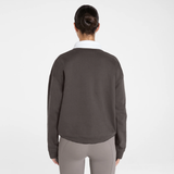 A woman viewed from behind wearing a dark brown long-sleeve cropped sweatshirt with a white collar, paired with gray leggings, against a light gray studio background.