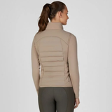 Pikeur AW26 Athleisure Quilted Flexvest Variant Mocha Cream. A woman shown from the back wearing a beige long-sleeve vest with horizontal quilted paneling on the back, paired with dark gray leggings, against a light gray studio background.