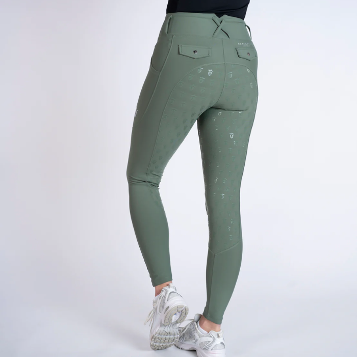 Green riding pants worn by a person on a white background
