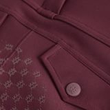 Close-up of a burgundy fabric garment detail showing a pocket with a matching button and a repeating tonal monogram pattern.