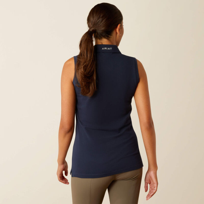 Woman wearing a navy sleeveless shirt with 'Ariat' branding on the back, standing against a beige background.