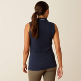 Woman wearing a navy sleeveless shirt with 'Ariat' branding on the back, standing against a beige background.