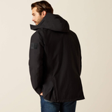 A man wearing a black hooded jacket, shown from a three-quarters back view against a plain beige studio background.