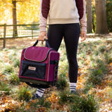 LeMieux AW26 Elite Pro Grooming Bag Varient Blackberry. A person outdoors in a park carrying a purple and black insulated cooler bag with a front pocket and top handle.