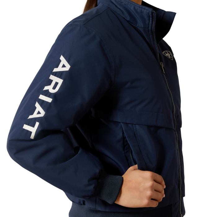 Ariat Youth 2.0 Insulated Stable Jacket Varient Navy. Close up of Ariat jacket with 'Ariat' branding down the sleeve in white, on a white background. 