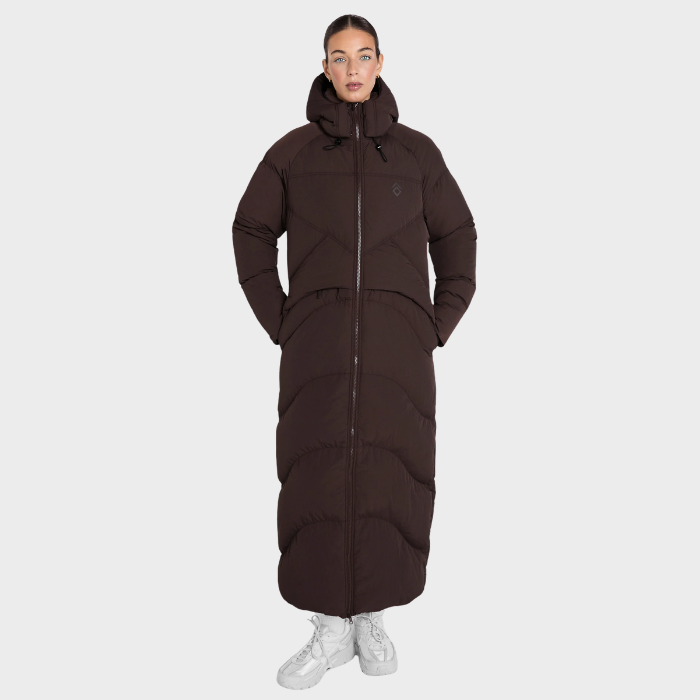 Aztec Diamond Matte Long Puffer AW26 Variant Espresso. A model wearing a long, dark brown puffer coat with a front zipper and hood, paired with white sneakers, against a solid light gray background.