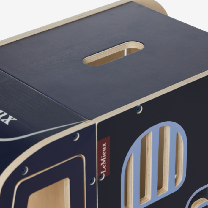 LeMieux AW26 Toy Pony Lorry Wooden Varient Brown. Close-up of a wooden box with a dark navy blue exterior, natural light wood edges, and a small red LeMieux brand label.