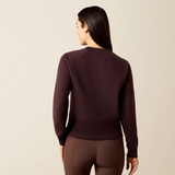 A woman shown from the back wearing a dark plum long-sleeve top and matching brown leggings against a plain light beige studio background.