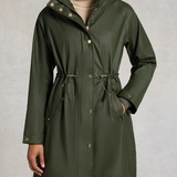Holland Cooper Chartwell Rain Parka Variant Hunter Green. An olive green hooded raincoat with gold-tone snap buttons and drawstring details, worn by a model against a textured gray background.