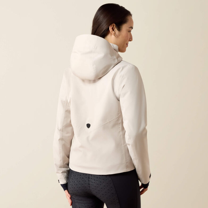 A woman shown from the back wearing a light cream hooded jacket and dark patterned leggings against a plain beige studio background.