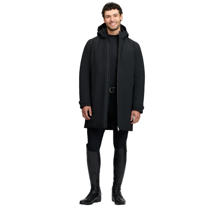 LeMieux AW26 Mens Waterproof Training Coat Varient Black. A man modeling a black hooded parka jacket with a front zipper, worn over a black outfit and tall black riding boots against a plain white background.