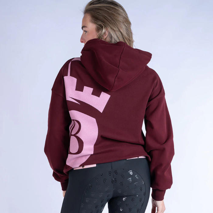 Person wearing a burgundy hoodie with a pink logo on the back against a white background