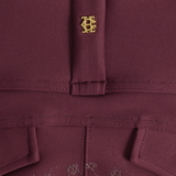 Close-up of a burgundy fabric garment featuring a gold embroidered monogram logo on the chest and matching embroidered details near the hem.