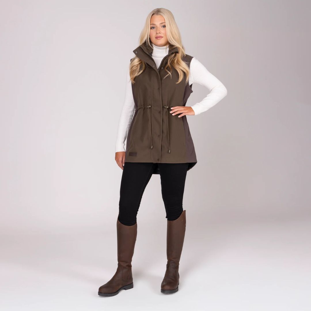 Woman wearing a brown gilet, white shirt, black leggings, and brown boots on a white background