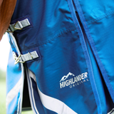 Close-up of a blue horse blanket with silver buckles and a white 'HIGHLANDER ORIGINAL' logo printed on the side.