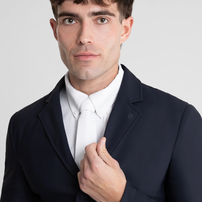 Man wearing a dark suit jacket over a white shirt on a light gray background