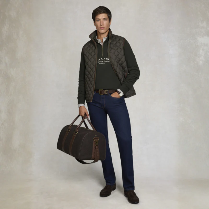 Male wearing gillet, jeans and holding a luggage bag