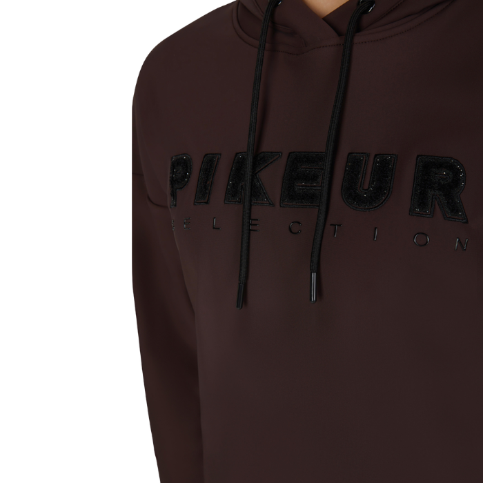 Pikeur AW26 Plushluxe Hoody Variant Chocolate/Brown. Close-up of a dark brown hoodie with black drawstrings and a black sequined 'PIKEUR COLLECTION' logo across the chest.