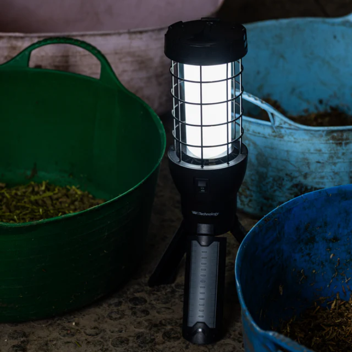 A black handheld LED bug light with a trippy base stands between green and blue buckets containing dried leaves or herbs.