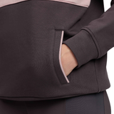Close-up of a dark charcoal gray/brown  fleece jacket with a light pink contrast trim and a side pocket, showing a hand in the pocket.