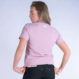 Person wearing a light pink polo shirt with a logo on the back, standing against a plain background.