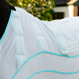 Close-up of a white horse rug with blue trim on a blurred outdoor background