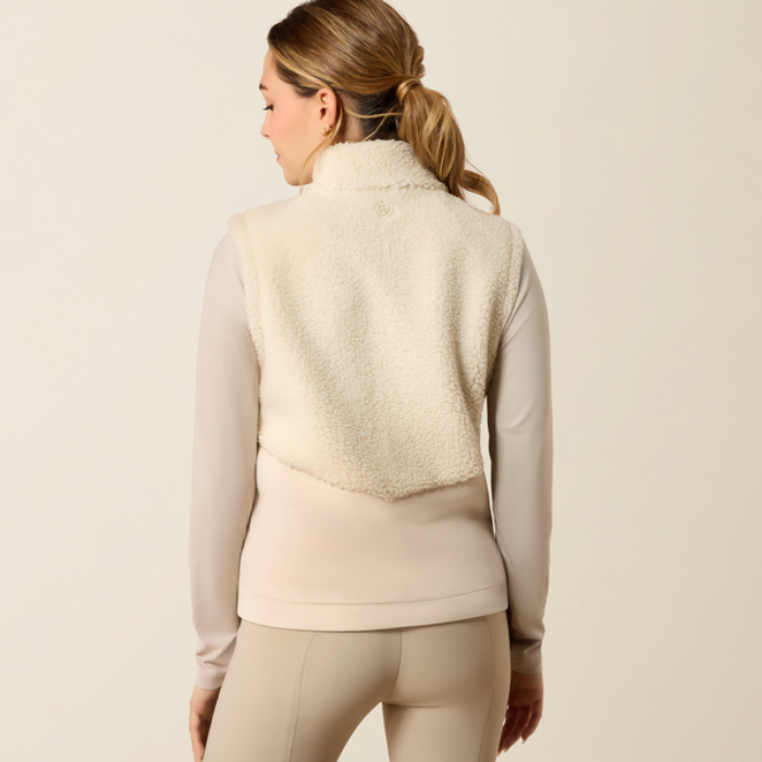 Ariat Yth Laviolette Full Zip Vest Varient Almond Milk. Lady wearing a cream fleece gilet with matching beige trousers from the back on a light background.