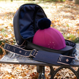 LeMieux AW26 Hat Bag Varient Blackberry. A pink LeMieux riding cap with a dark navy blue pom-pom sits inside an open navy blue equestrian saddlebag. The bag features a wide, adjustable navy blue shoulder strap with 'LE MIEUX' branding printed in white. 