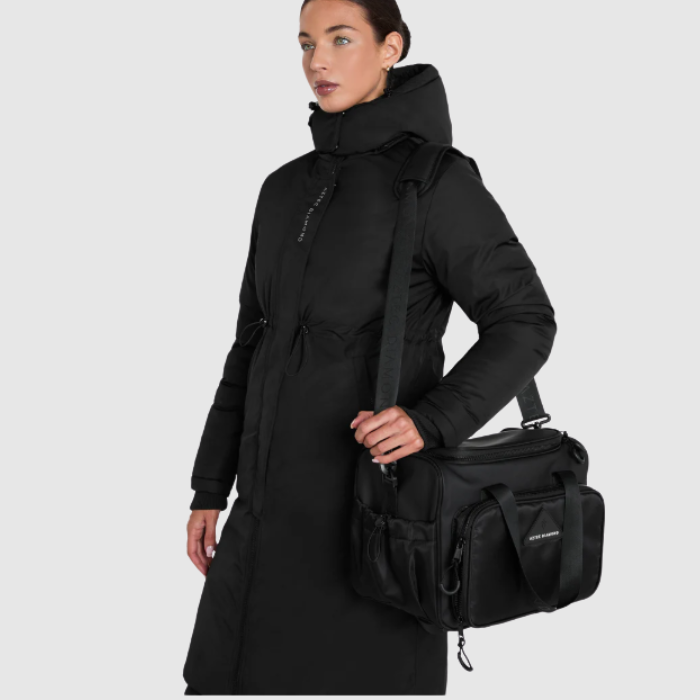 Woman wearing a black coat holding a black bag on a light grey background