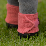LeMieux AW26 Toy Pony Bandages Variant Colour Spiced Earth.
Close-up of a toy ponies lower legs wearing pink fleece booties with black rubber soles, standing on green grass.
