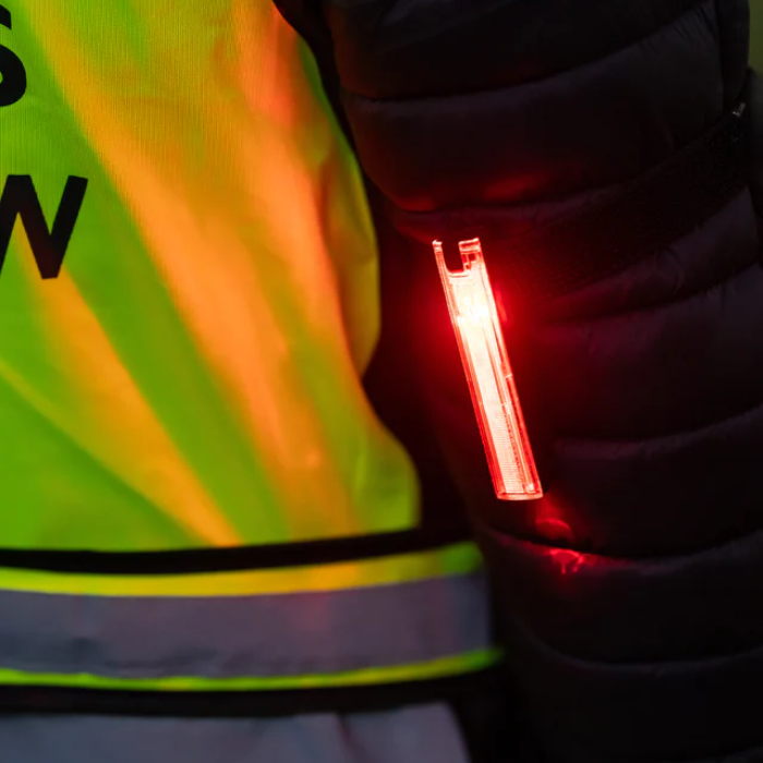 Person wearing a high-visibility safety vest with a red light attached, likely for safety purposes.