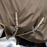 LeMieux AW26 Arika Ripstop 0g Turnout Rug Varient Alpine. Close-up of a brown waterproof rug with adjustable straps and striped trim details.