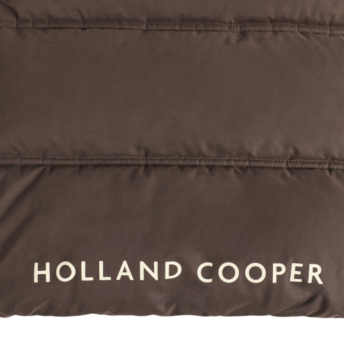 Holland Cooper Cranborne Training Gilet Variant Chocolate. Close-up of a dark brown puffer jacket fabric with horizontal quilting and the brand name 'HOLLAND COOPER' printed in white at the bottom.