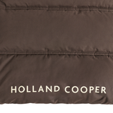Holland Cooper Cranborne Training Gilet Variant Chocolate. Close-up of a dark brown puffer jacket fabric with horizontal quilting and the brand name 'HOLLAND COOPER' printed in white at the bottom.