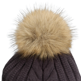 Close-up of a knit beanie with a large fluffy tan faux-fur pom-pom on a white background.