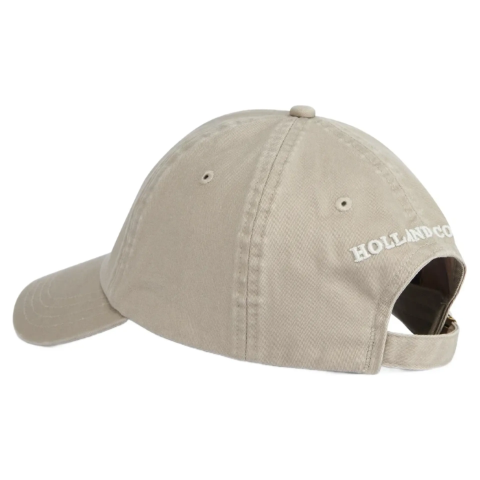 A light beige cotton baseball cap shown from a side-back angle, featuring white embroidered text reading 'HOLLAND COOPER' on the back and an adjustable back strap.