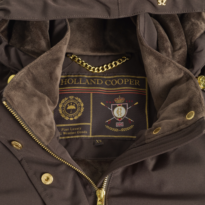 Holland Cooper Essential Waterproof Jacket Variant Bournville. Close-up of a brown jacket opening showing a dark brown interior lining, gold-tone zipper and snaps, and a visible Holland Cooper neck label with a chain detail.