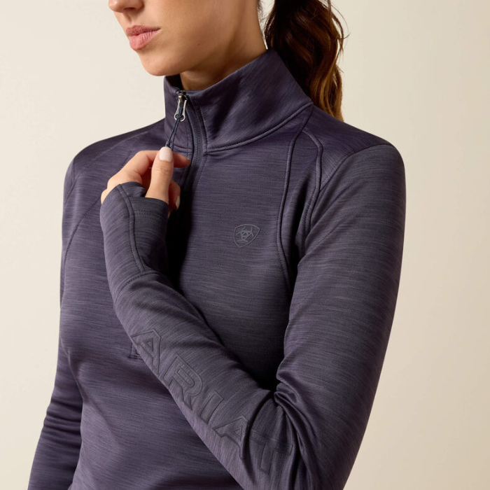 Ariat Ladies Team EQ 1/2 Zip Pullover Variant Odyssey Grey. A close-up of a woman wearing a dark purple long-sleeve athletic quarter-zip top, showing the zipper, textured fabric, and a subtle embroidered logo on the chest.