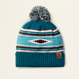 Ariat Ladies Serape Beanie Varient Teal Serape. Teal knit beanie with pattern and pom-pom on a beige background