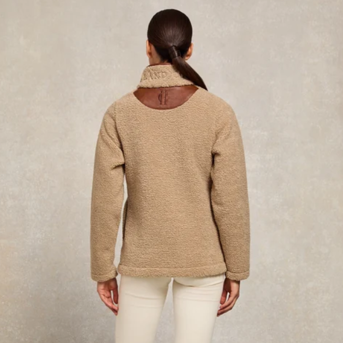 Holland Cooper Ladies Country Fleece Quarter Zip Variant Natural Borg. A woman viewed from the back wearing a beige sherpa fleece sweater with a brown collar trim and white pants, set against a textured light gray studio background.