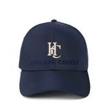 A navy blue baseball cap with an embroidered white 'HC' monogram and 'HOLLAND COOPER' text on the front, set against a plain white background.